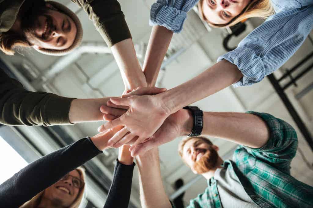 Employer Branding: Kollegen im Büro halten sich an Händen und zeigen starken Zusammenhalt